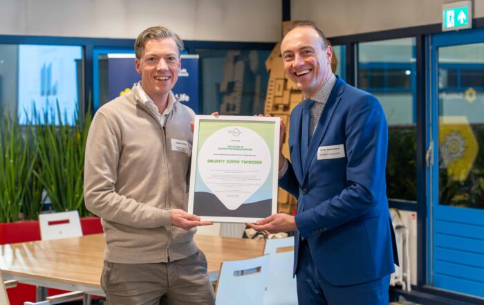 Twee lachende mannen met ingelijste smurfit oorkonde in de hand