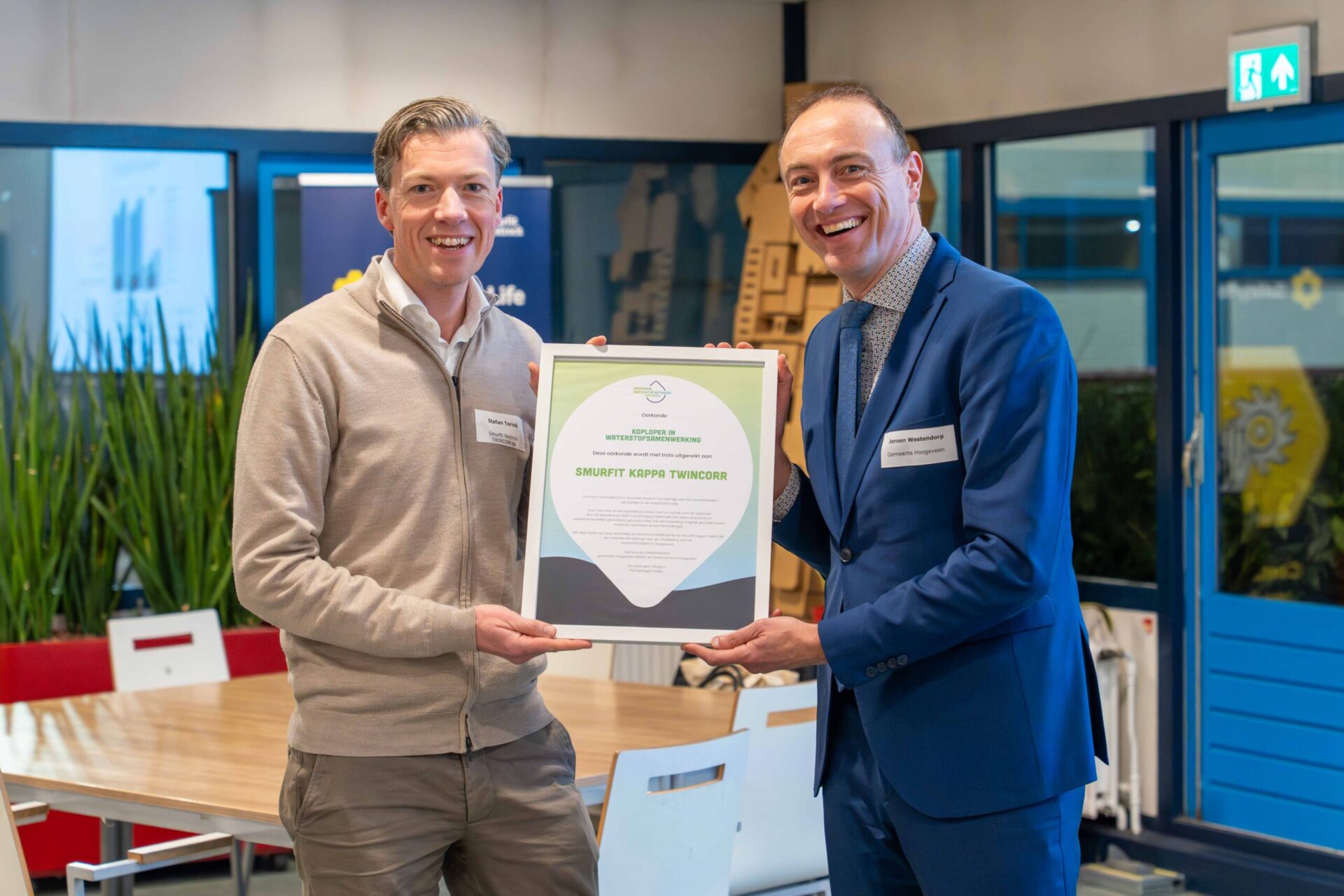 Twee lachende mannen met ingelijste smurfit oorkonde in de hand